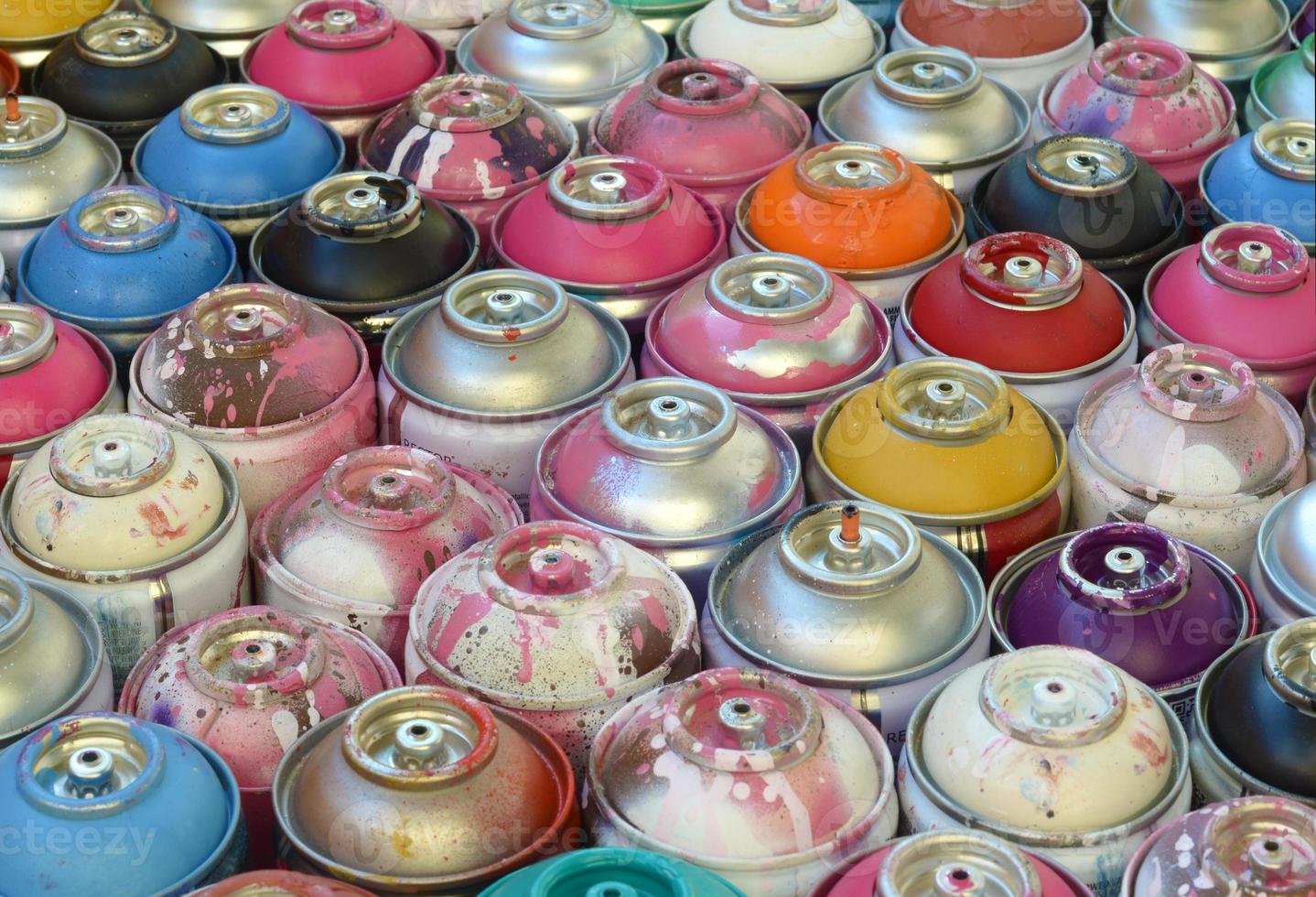 Large number of used colorful spray cans of aerosol paint lying on the treated wooden surface in the artist's graffiti workshop close up. Dirty and stained cans for art photo