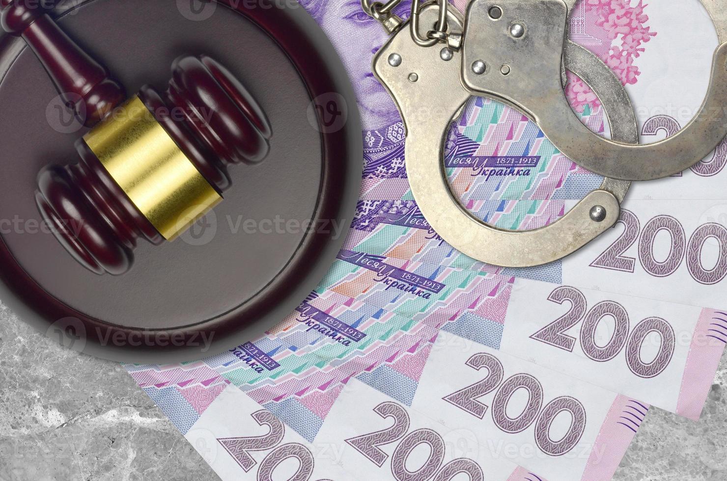 200 Ukrainian hryvnias bills and judge hammer with police handcuffs on court desk. Concept of judicial trial or bribery. Tax avoidance photo