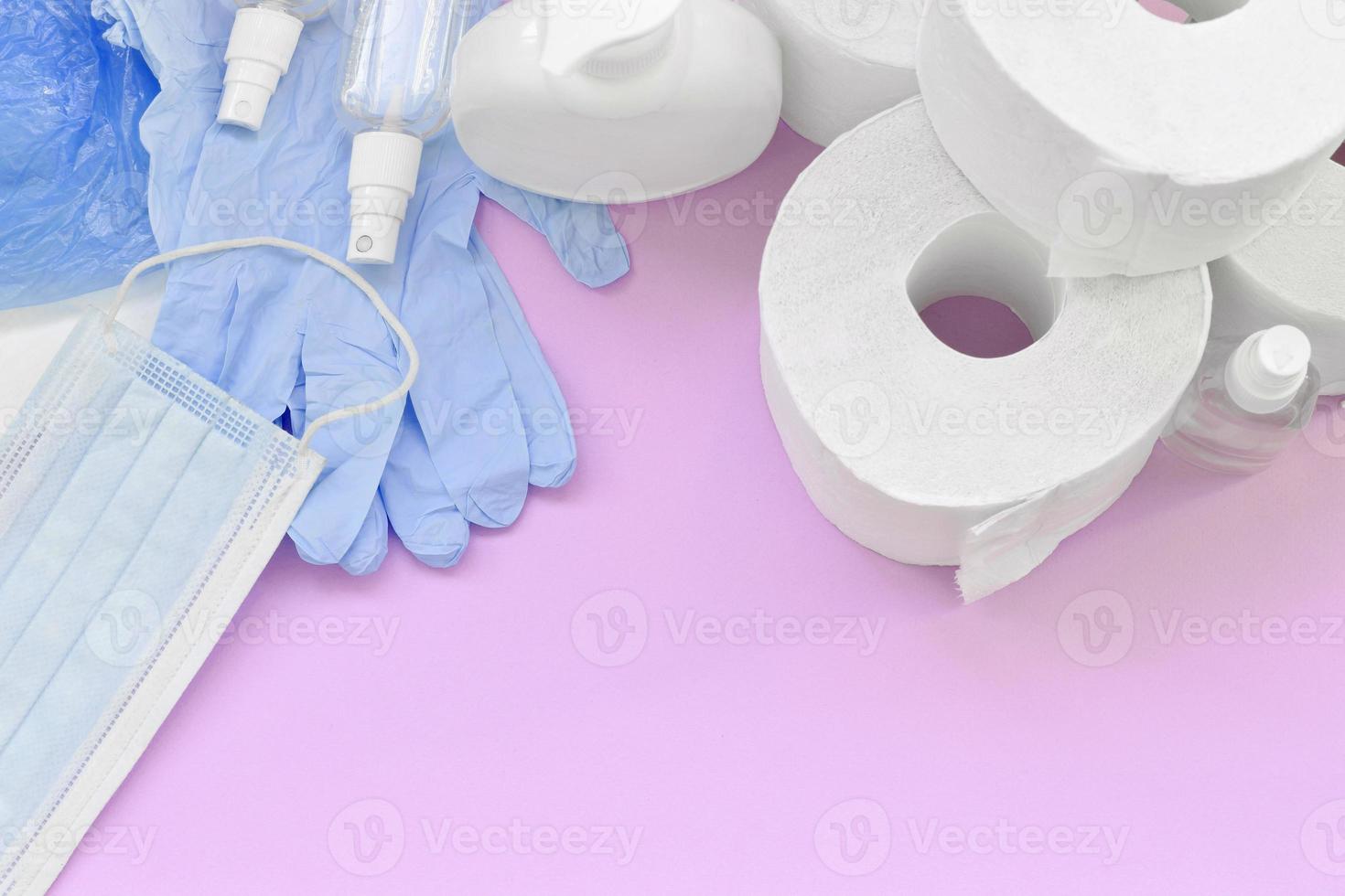 Set of important items for Covid-19 quarantine. Toilet paper, rubber disposable gloves with surgical face mask and hand sanitizer with liquid soap bottle on lilac background photo