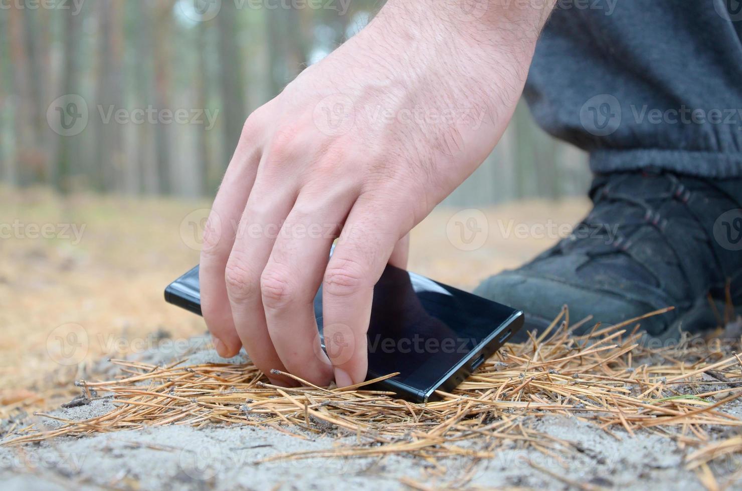 Male hand picking up lost mobile phone from a ground in autumn fir wood path. The concept of finding a valuable thing and good luck photo