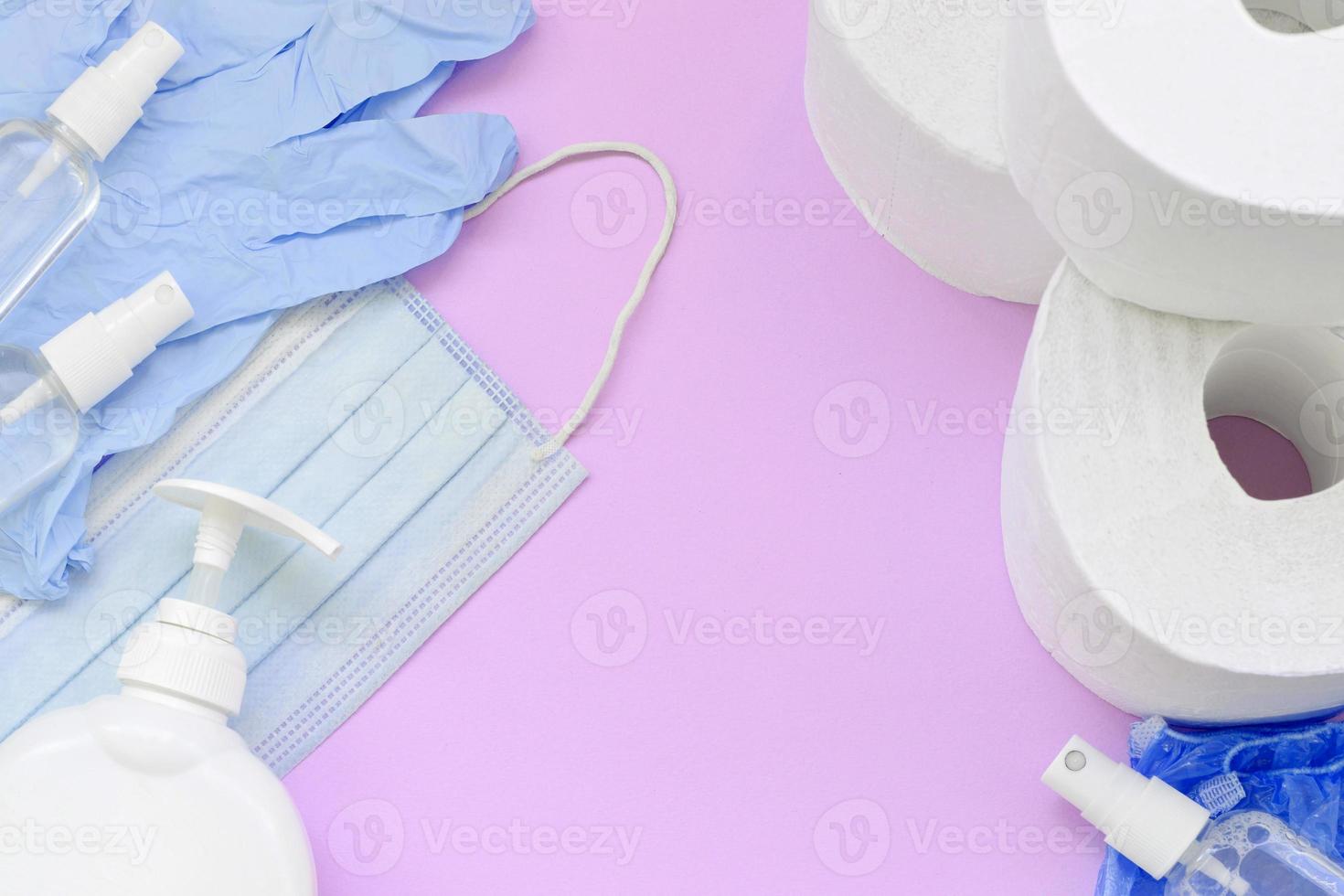 Set of important items for Covid-19 quarantine. Toilet paper, rubber disposable gloves with surgical face mask and hand sanitizer with liquid soap bottle on lilac background photo