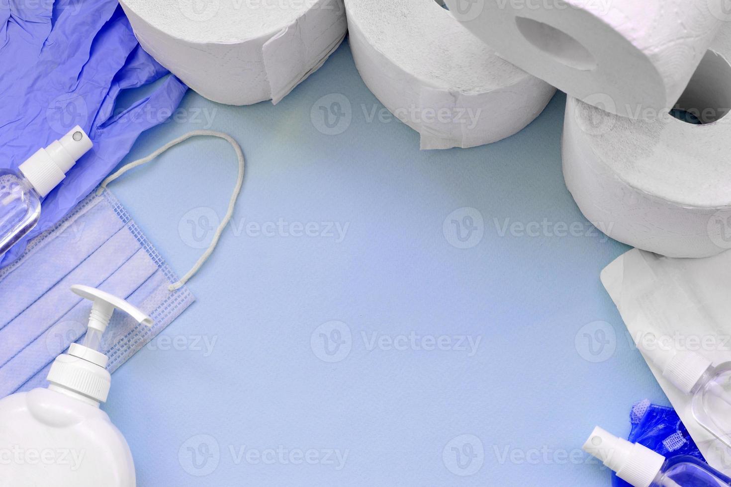 Set of important items for Covid-19 quarantine. Toilet paper, rubber disposable gloves with surgical face mask and hand sanitizer with liquid soap bottle on blue background photo