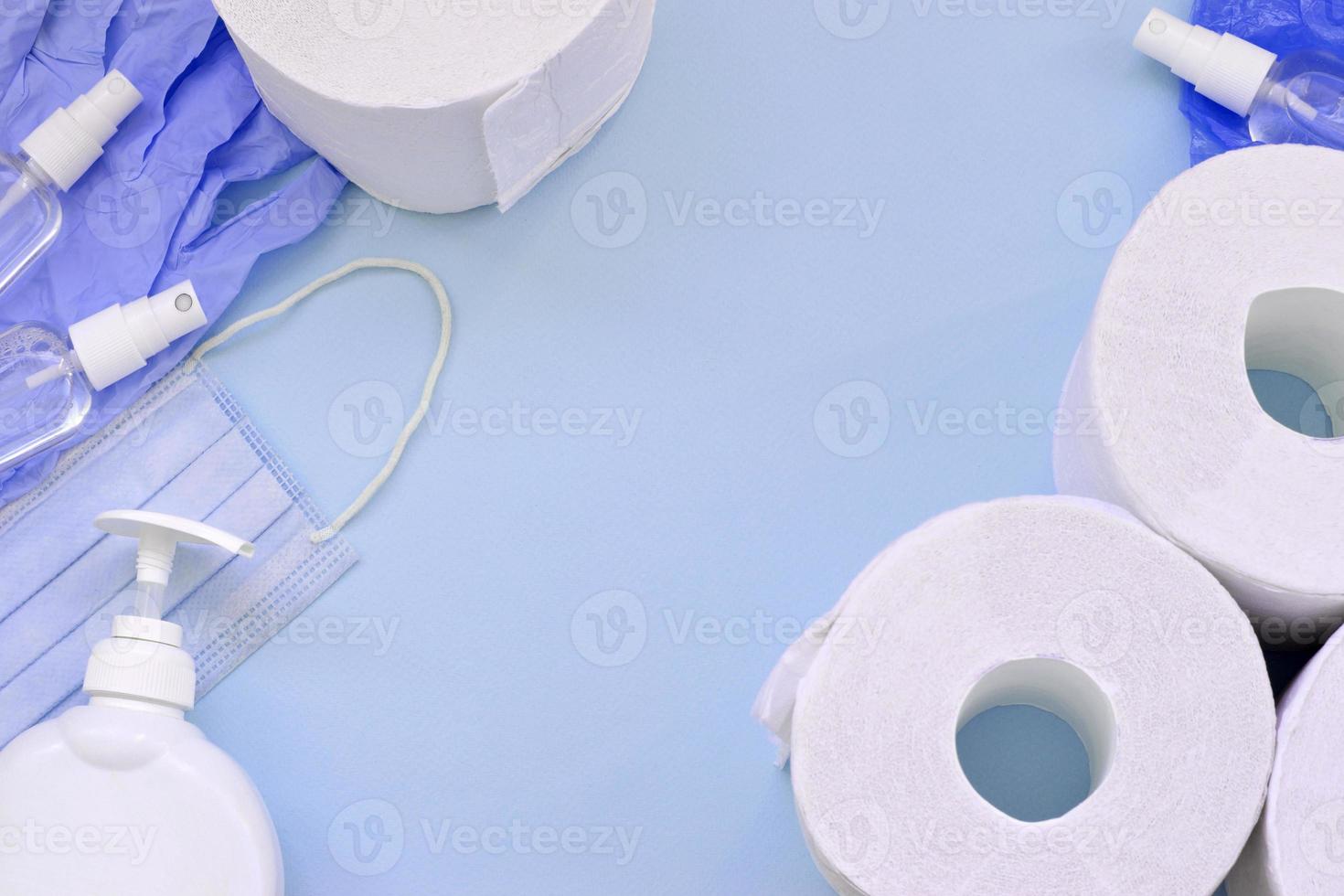 Set of important items for Covid-19 quarantine. Toilet paper, rubber disposable gloves with surgical face mask and hand sanitizer with liquid soap bottle on blue background photo