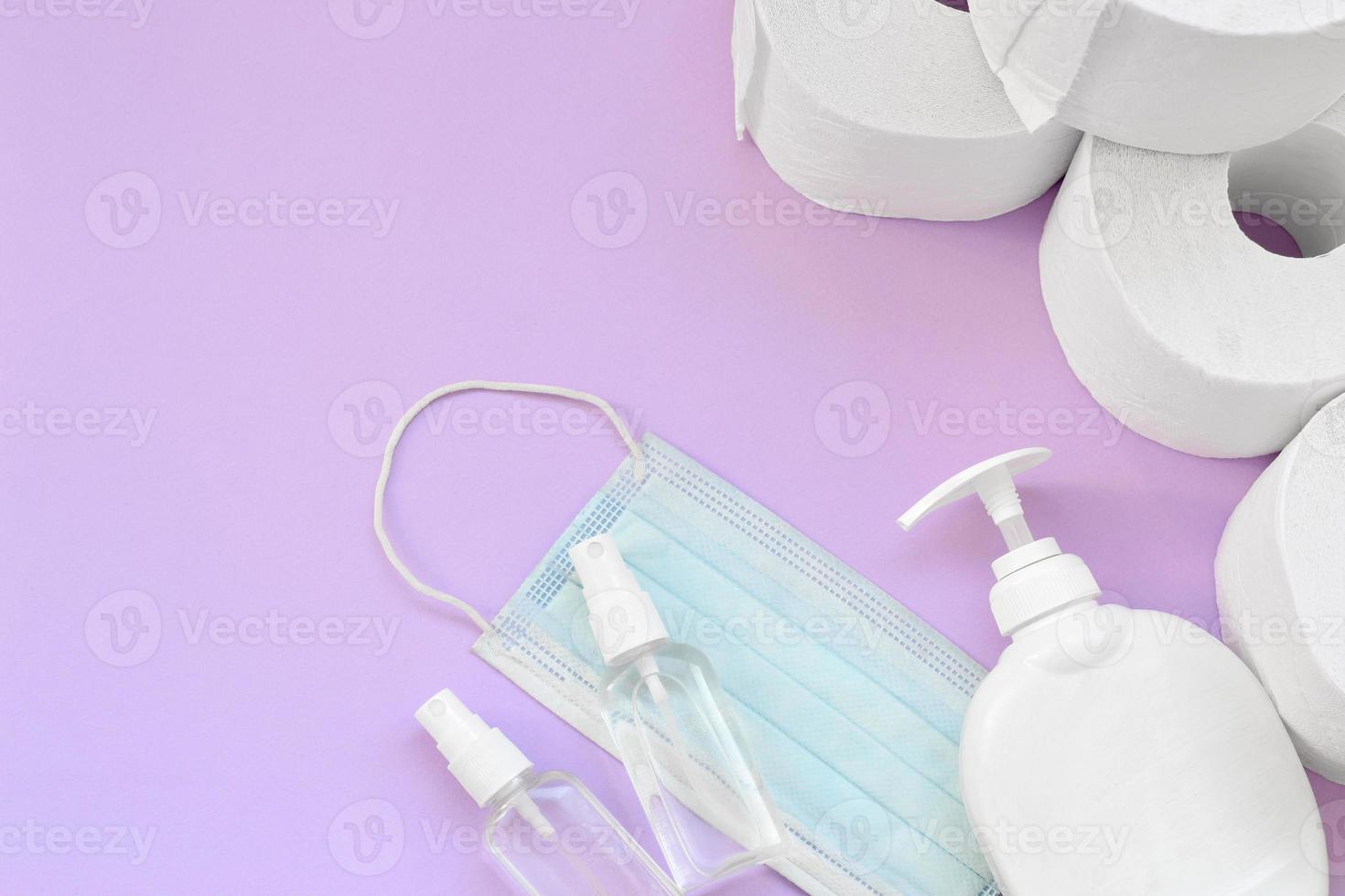 Set of important items for Covid-19 quarantine times. Toilet paper with surgical face mask and hand sanitizer with liquid soap bottle on lilac background photo