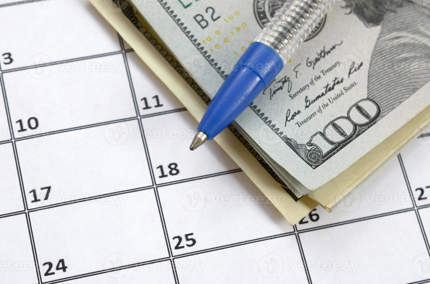 Pen and many hundred US dollar bills on calendar page close up photo