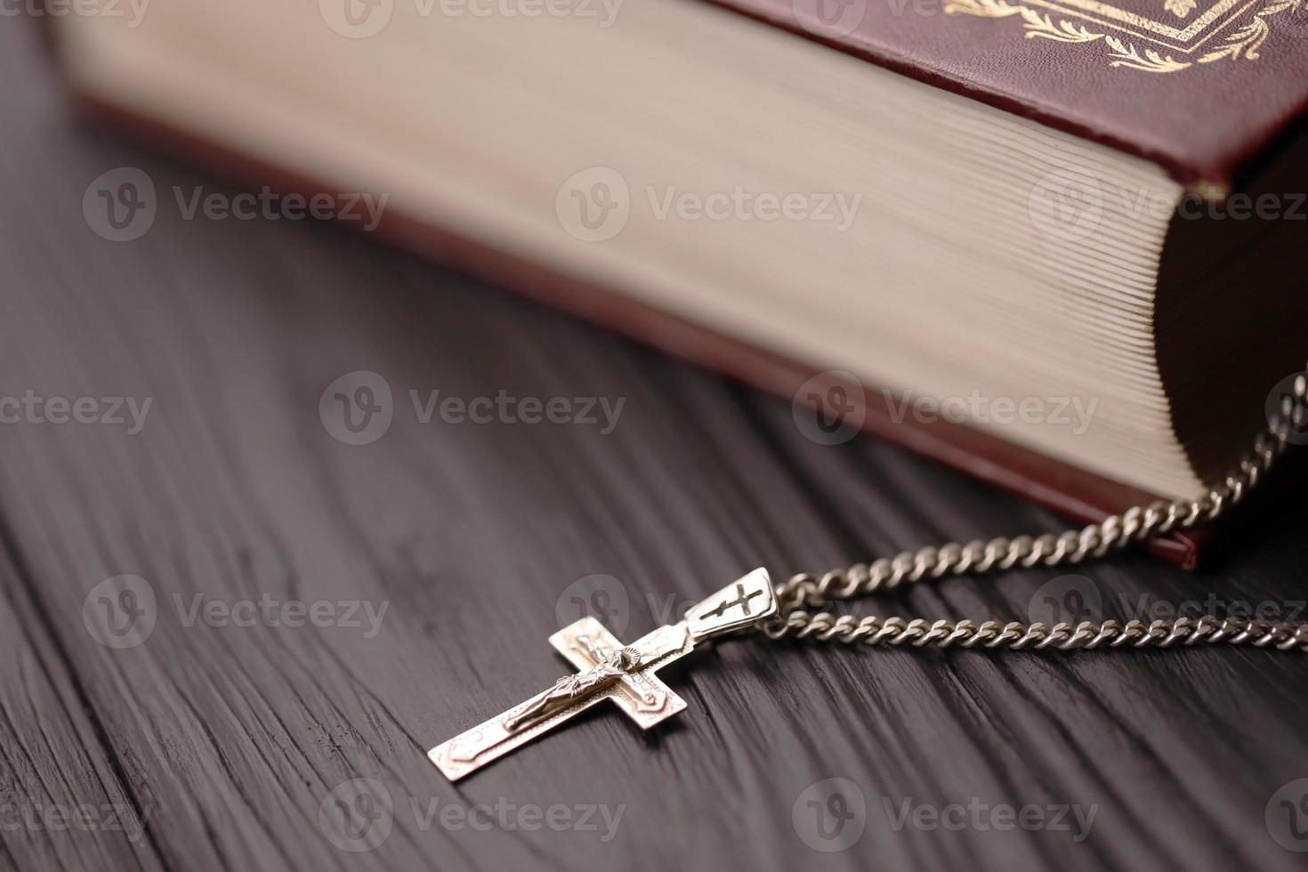 collar de plata con cruz crucifijo en el libro de la santa biblia cristiana sobre una mesa de madera negra. pidiendo bendiciones de dios con el poder de la santidad, que trae suerte foto