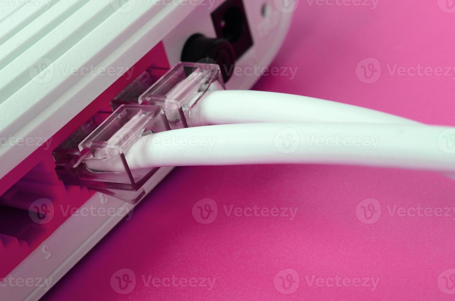 The Internet cable plugs are connected to the Internet router, which lies on a bright pink background. Items required for Internet photo