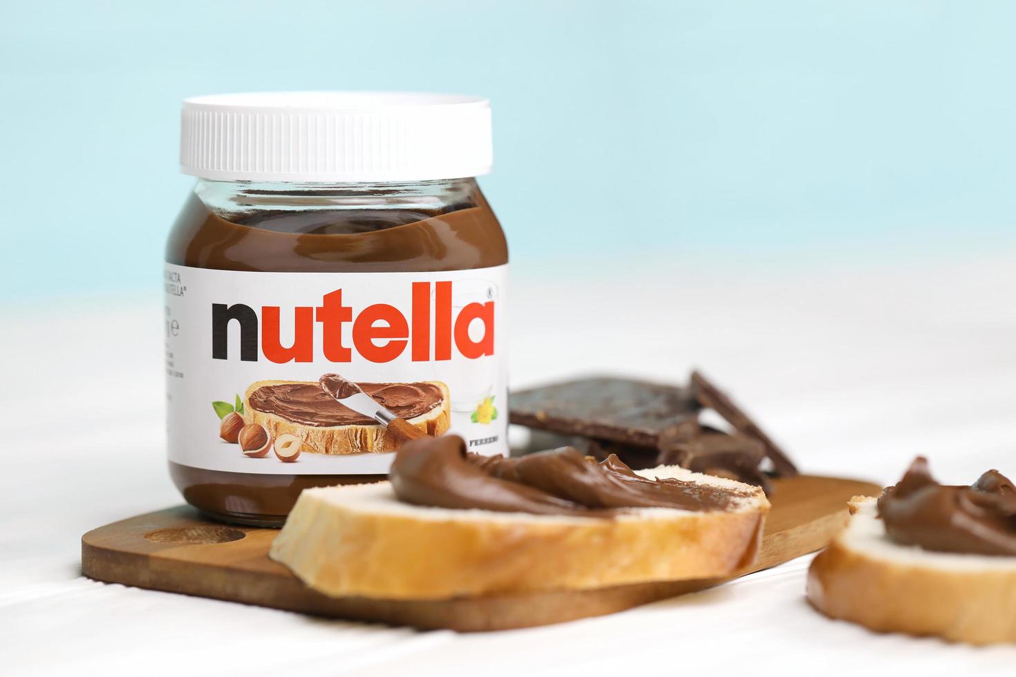 KHARKOV, UKRAINE - DECEMBER 27, 2020 Nutella glass can and spread on freshly baked bread. Nutella is manufactured by Italian company Ferrero first introduced in 1964 photo