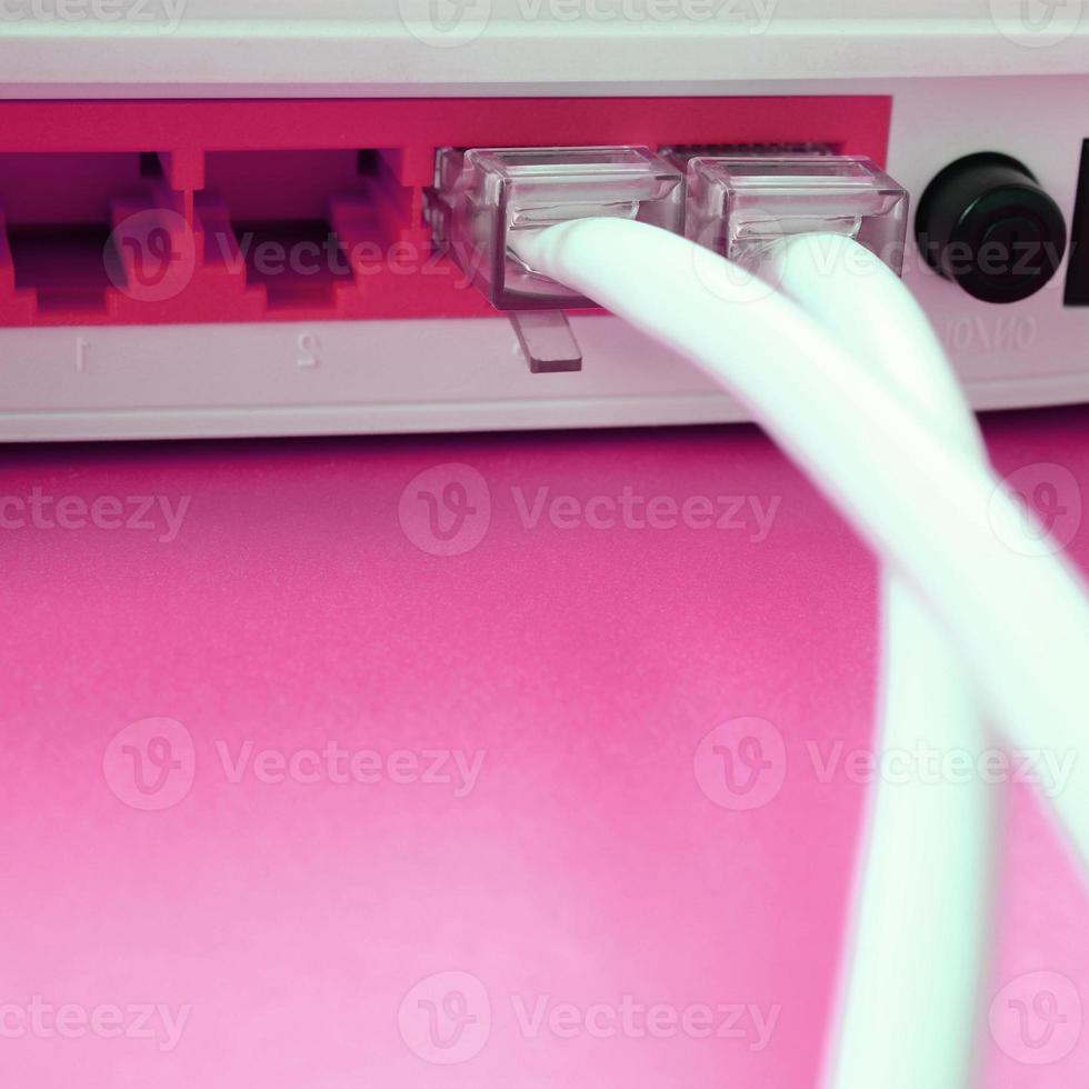 los enchufes del cable de Internet están conectados al enrutador de Internet, que se encuentra sobre un fondo rosa brillante. elementos necesarios para internet foto