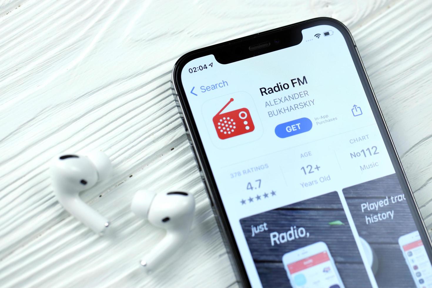 KHARKOV, UKRAINE - MARCH 5, 2021 Radio fm icon and application from App store on iPhone 12 pro display screen with airpods pro on white table photo