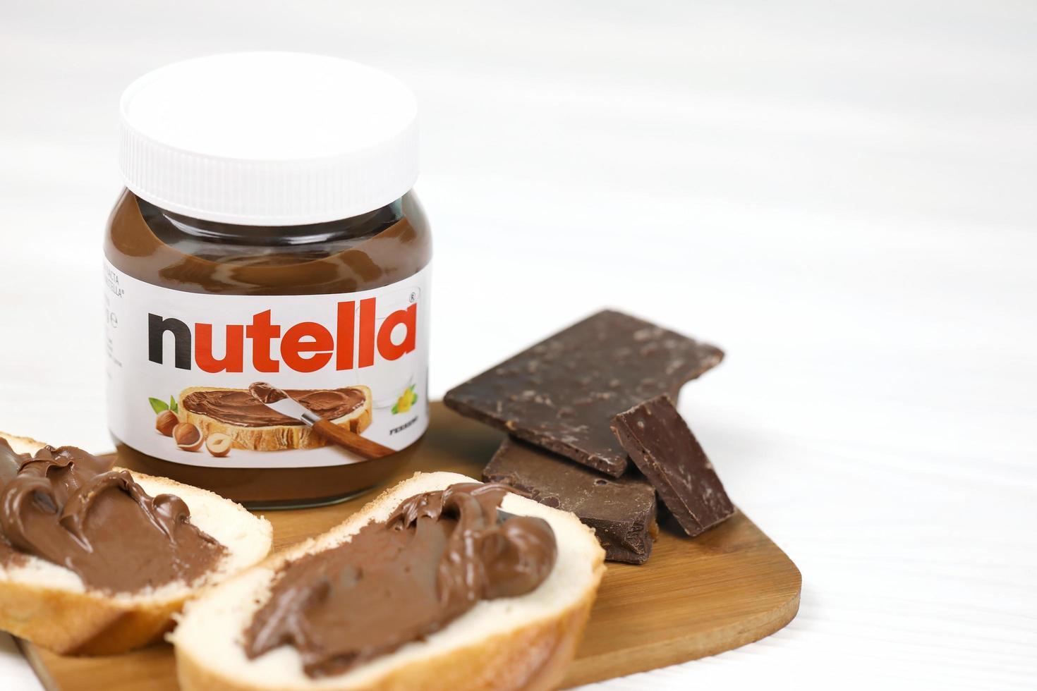 kharkov, ucrania - 27 de diciembre de 2020 lata de vidrio de nutella y untada en pan recién horneado. nutella es fabricada por la empresa italiana ferrero introducida por primera vez en 1964 foto