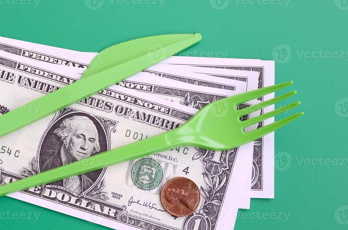 Disposable plastic cutlery green. Plastic fork and knife lie on a small amount of US dollars photo