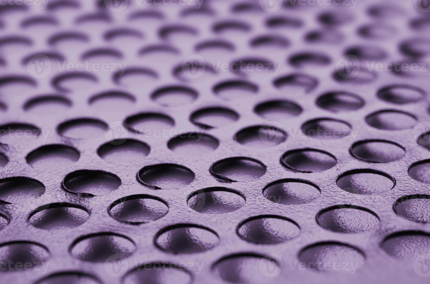 Black metal computer case panel mesh with holes on purple background. Abstract close up photo