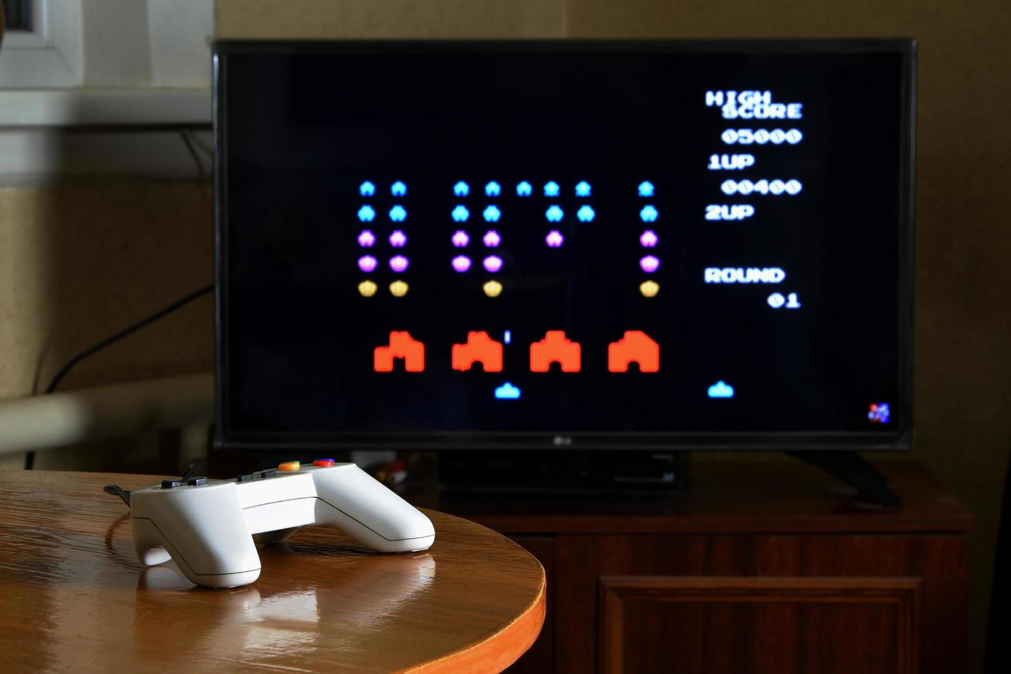 KHARKOV, UKRAINE - NOVEMBER 12, 2020 Dendy video game controller on table with Space invaders game on display photo