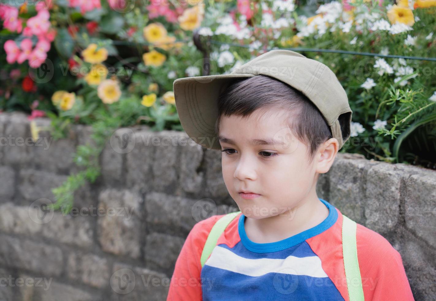Portrait kid boy looking out with thinking face,Child wearing cap hat and carrying backpack enjoying time in the park,Children exploring with nature on School camp concept photo