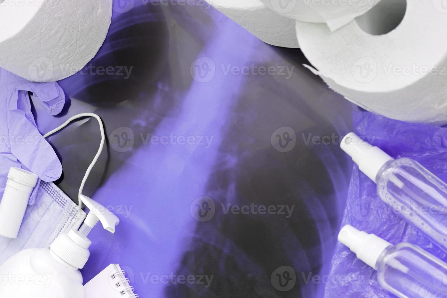 Set of important items for Covid-19 quarantine. Toilet paper, rubber disposable gloves with surgical face mask and hand sanitizer with liquid soap bottle on human chest x-ray film photo