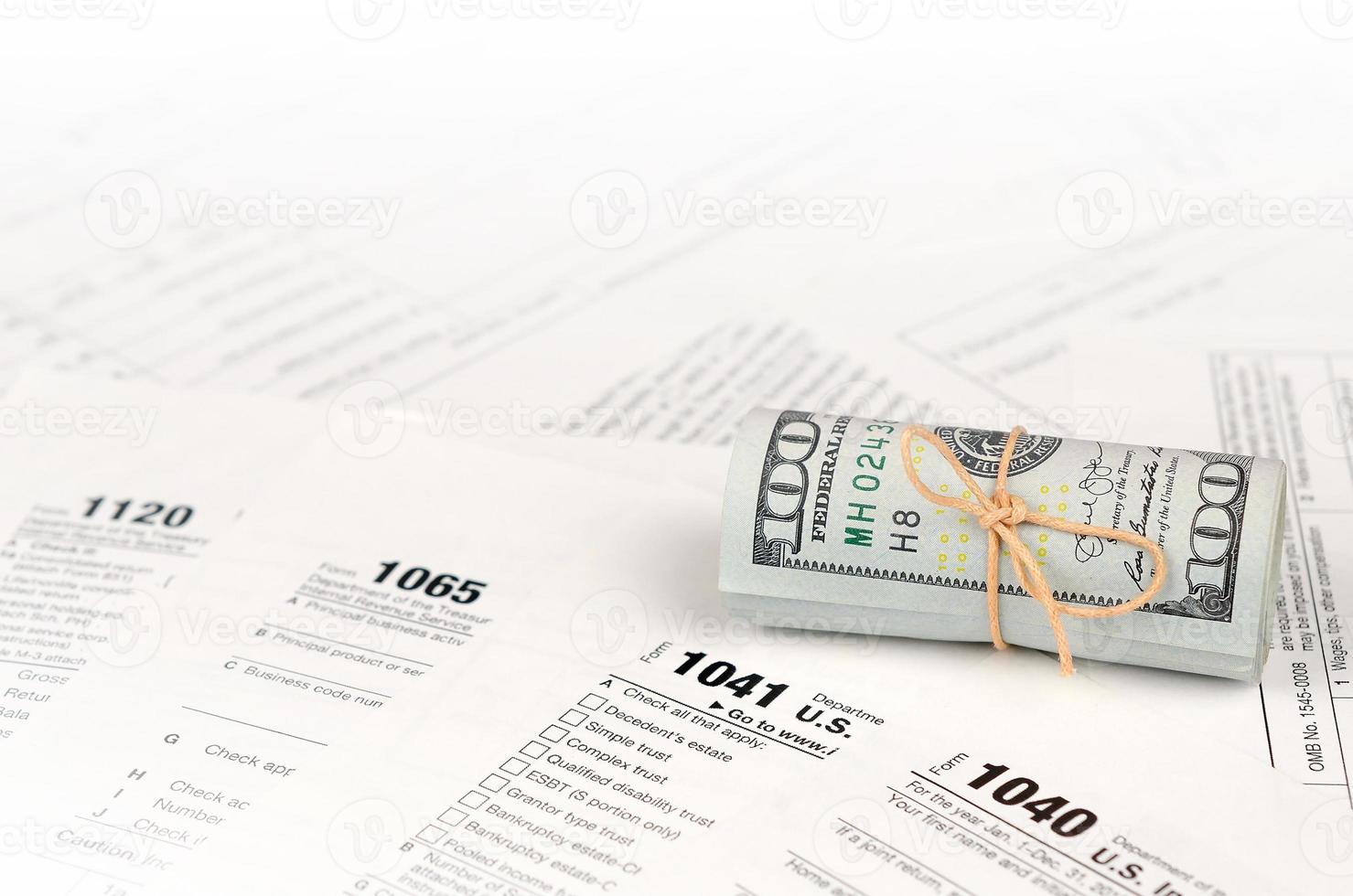 Tax forms lies near roll of hundred dollar bills. Income tax return photo