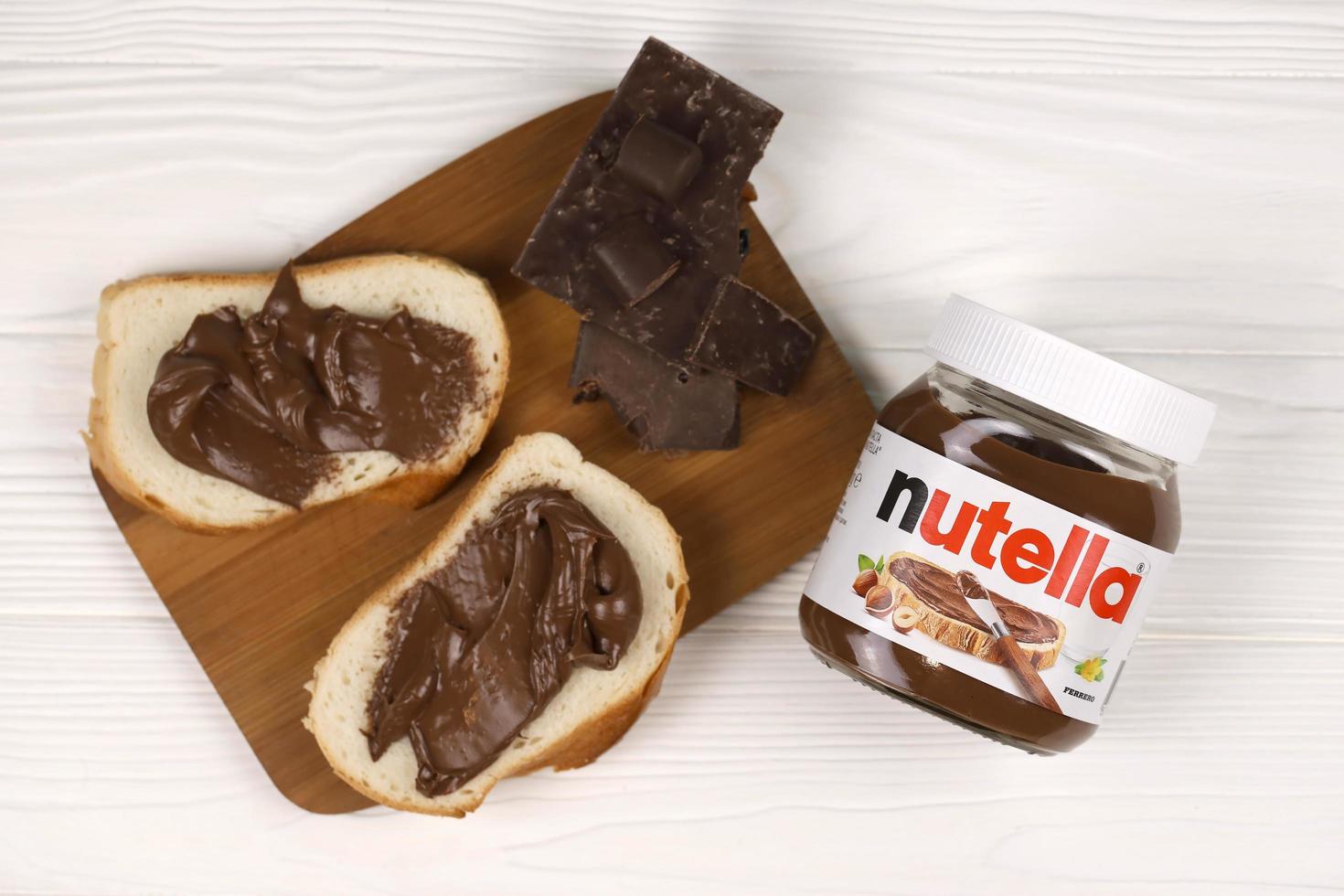 KHARKOV, UKRAINE - DECEMBER 27, 2020 Nutella glass can and spread on freshly baked bread. Nutella is manufactured by Italian company Ferrero first introduced in 1964 photo