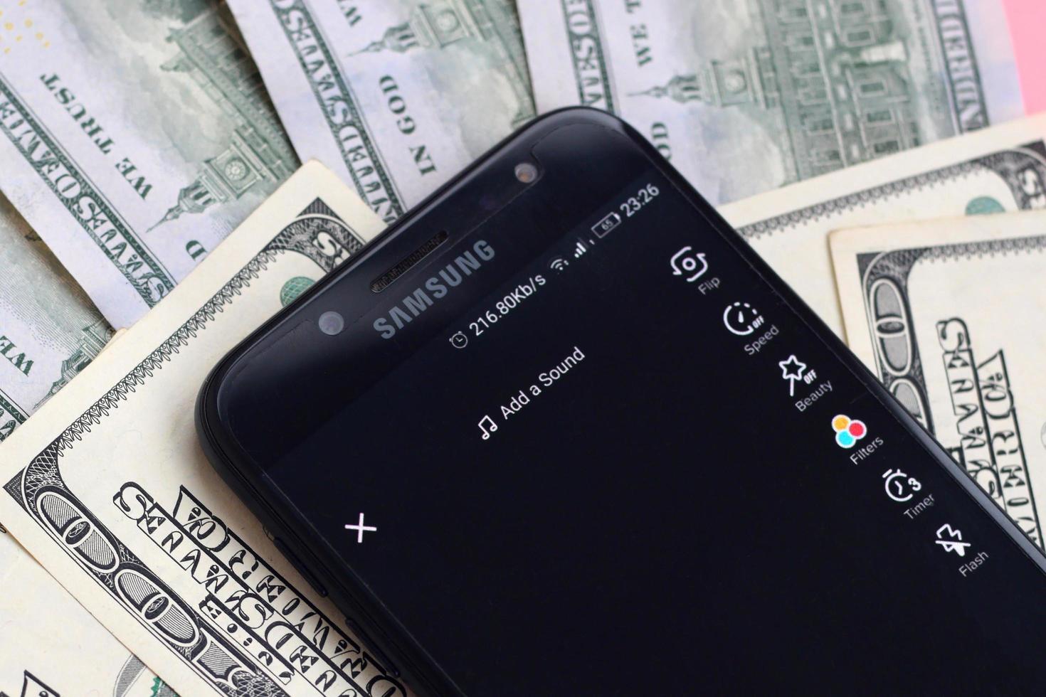 Smartphone screen with Tiktok app and lot of hundred dollar bills. Business and social networking concept photo