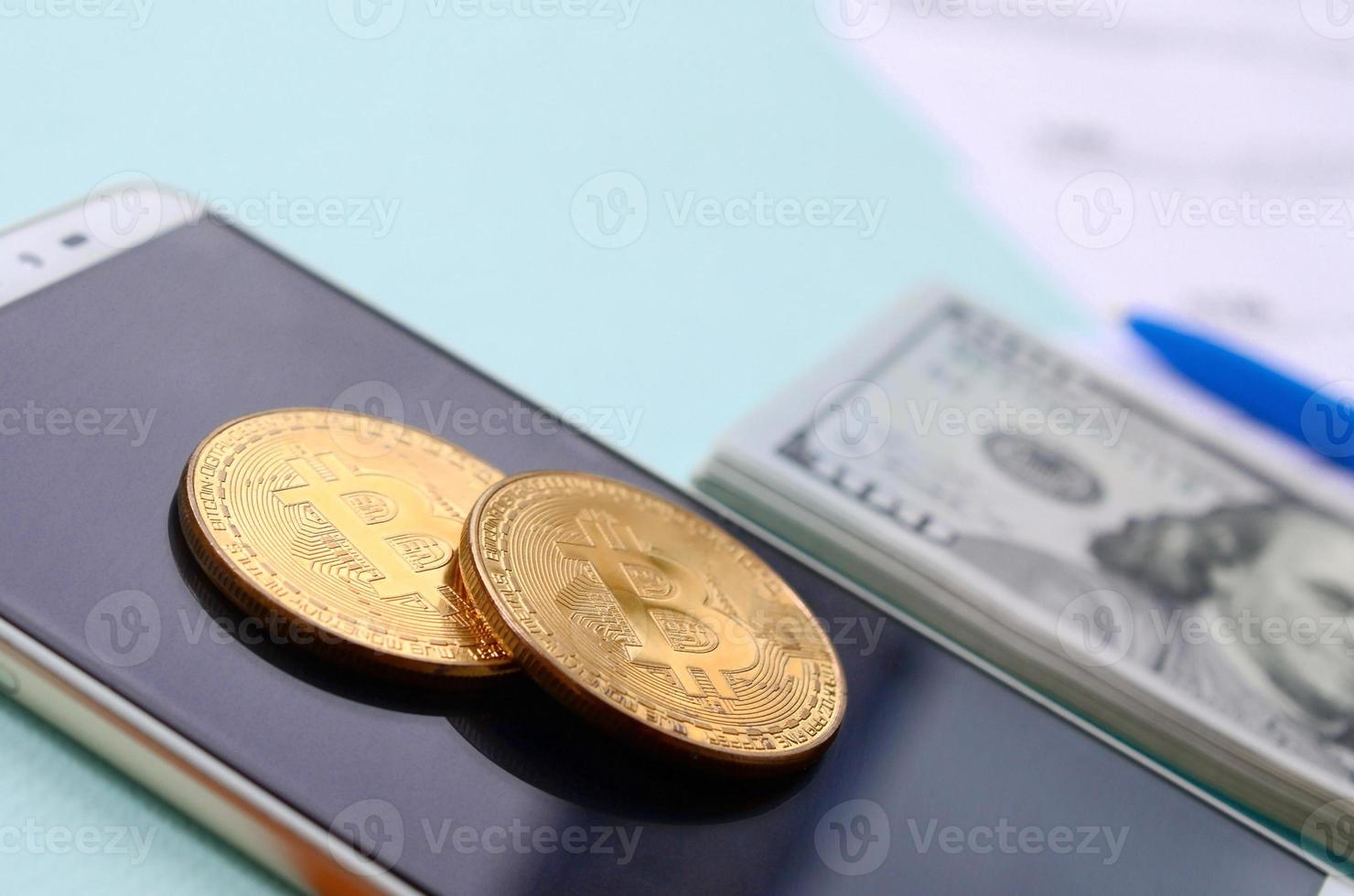 Bitcoins lies with the tax forms, hundred dollar bills and smartphone on a light blue background. Income tax return photo