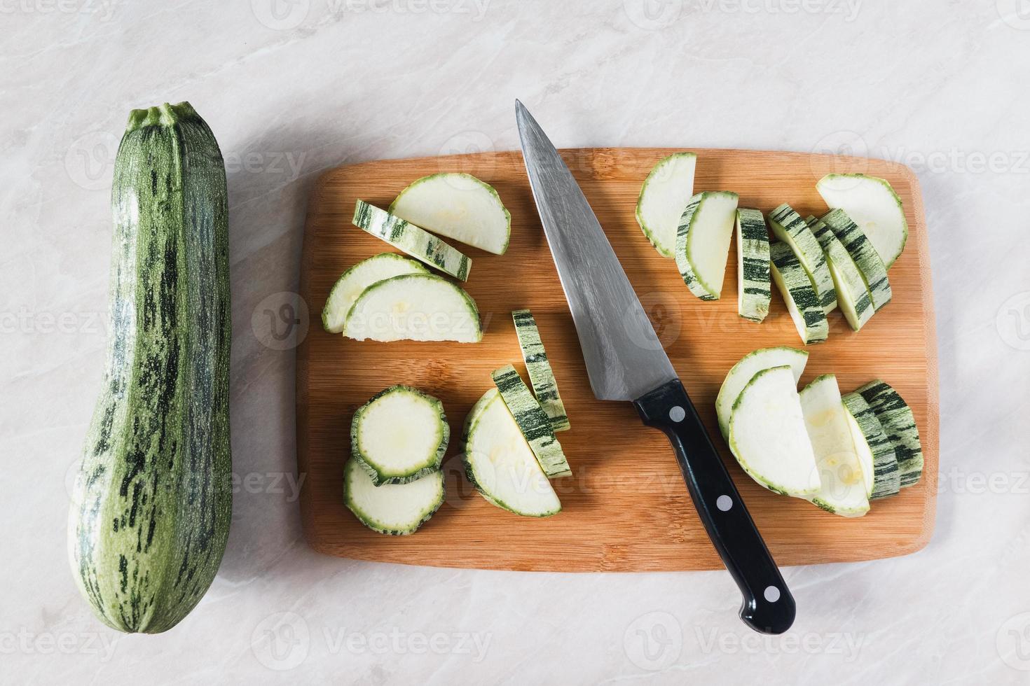 Cutting zucchini on wooden board, whole squash, knife and slices, overhead view photo