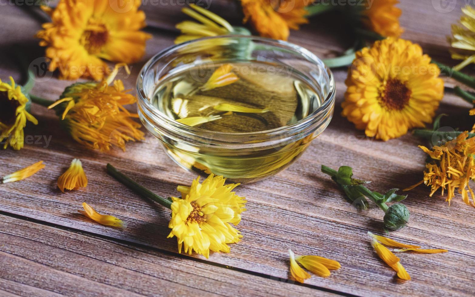 Calendula officinalis cosmetic oil, dried and fresh marigold flowers on wooden table photo