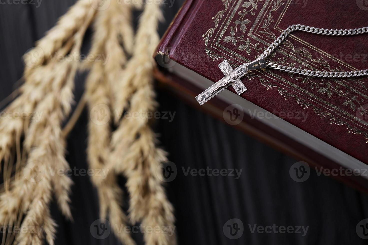 collar de plata con cruz crucifijo en el libro de la santa biblia cristiana sobre una mesa de madera negra. pidiendo bendiciones de dios con el poder de la santidad foto