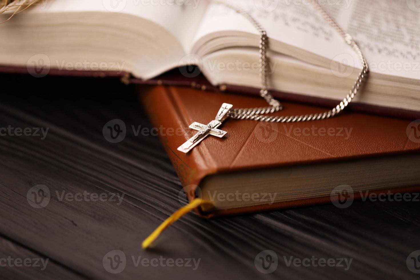 Silver necklace with crucifix cross on christian holy bible book on black wooden table. Asking blessings from God with the power of holiness, which brings luck photo