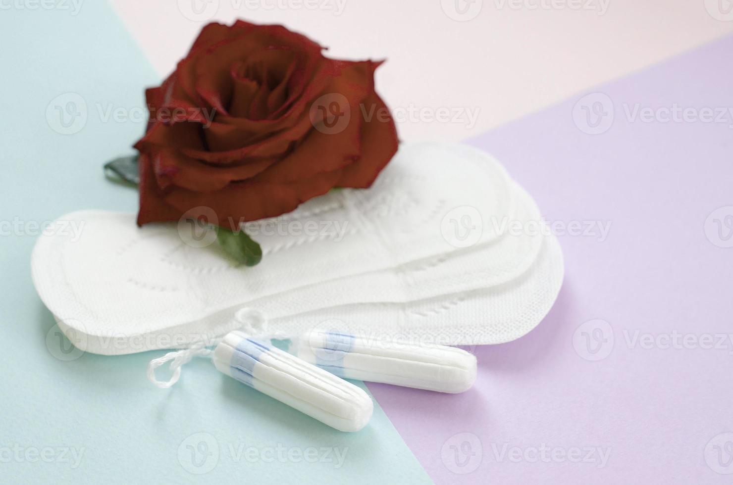 Menstrual pads and tampons with red rose flower on multicolored background photo