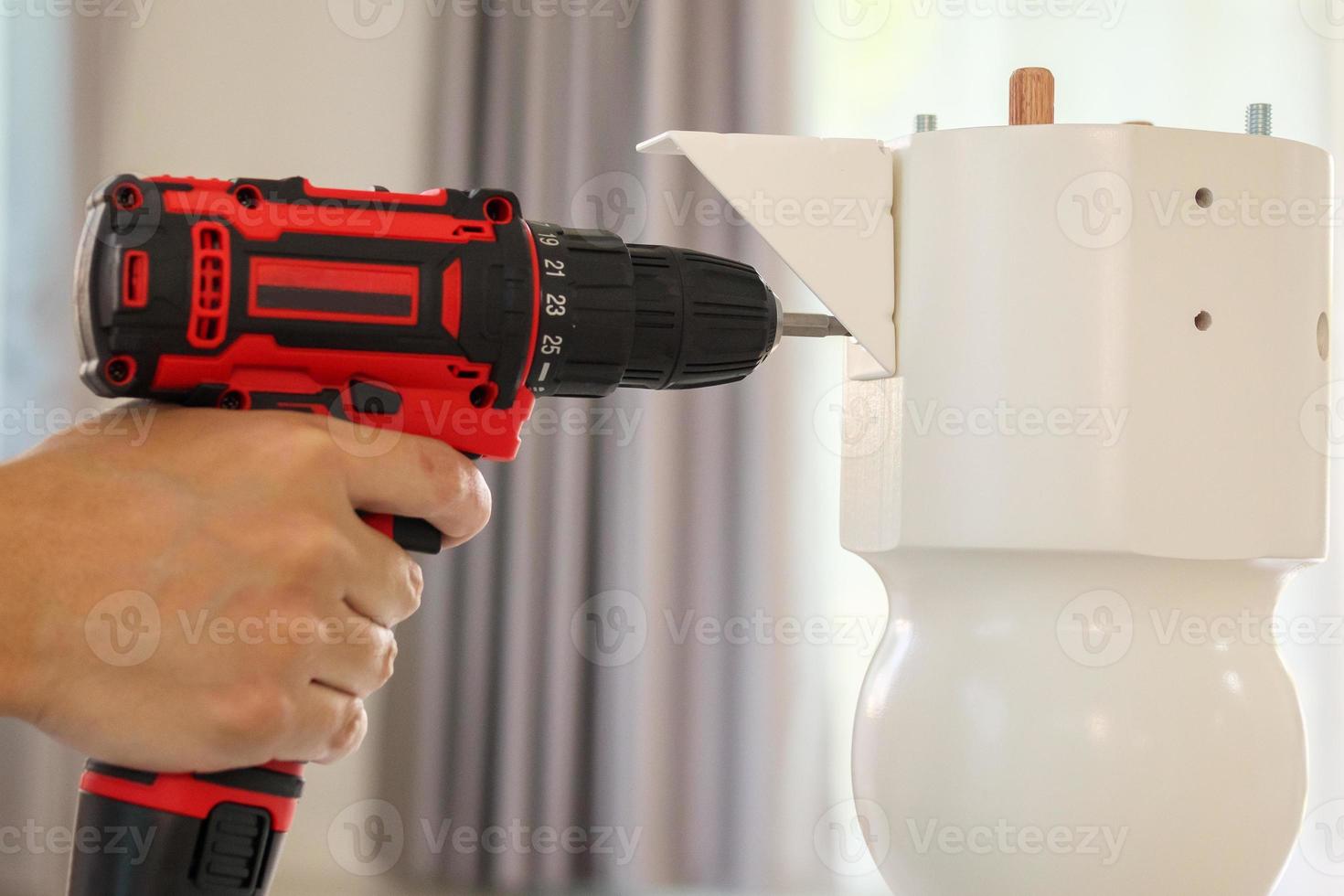 man assembling white table furniture at home using cordless screwdriver photo