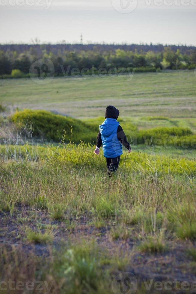 Children in the open spaces of the field are walking among the juicy spring grass in the light of sunset along a narrow trampled path photo