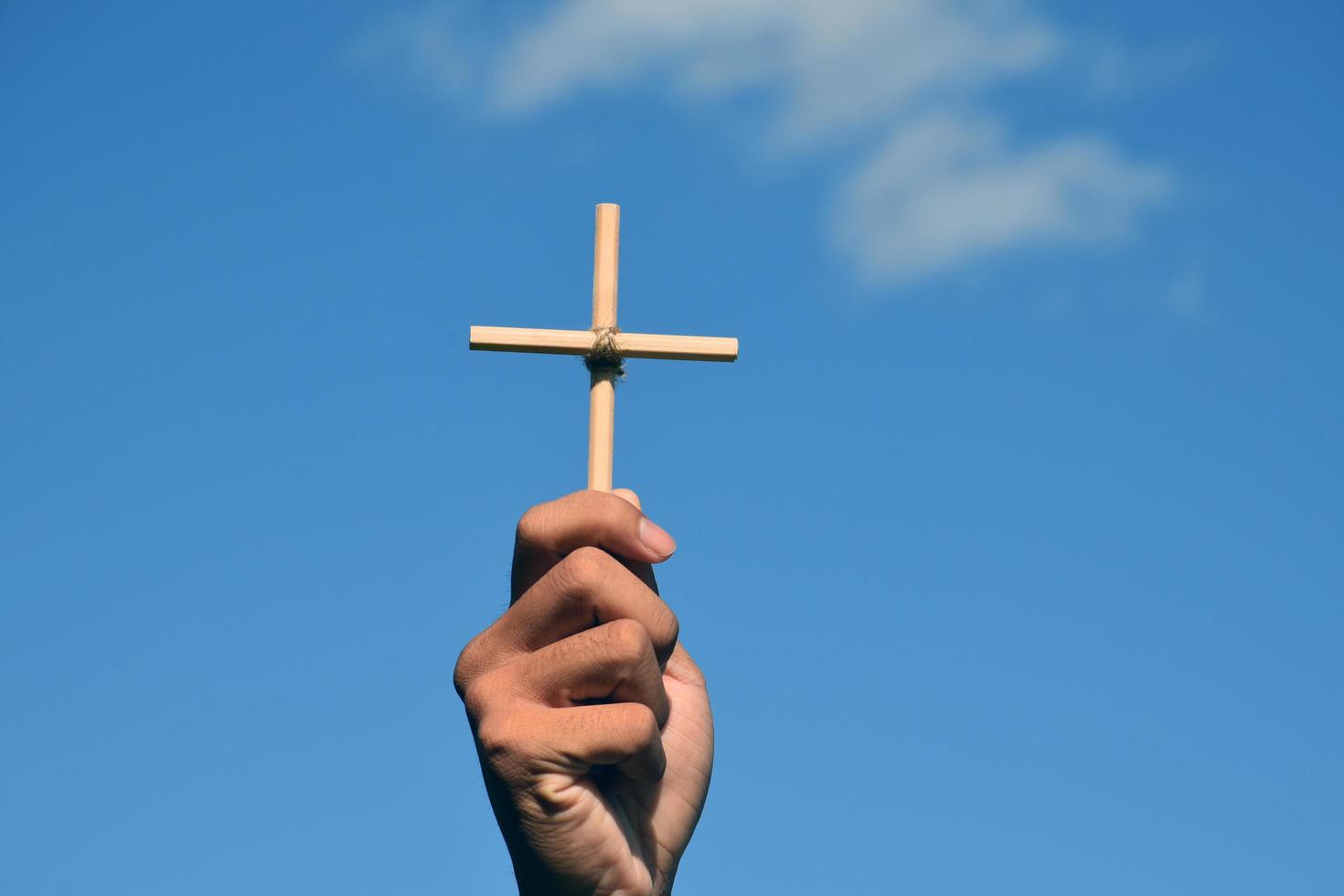pequeña cruz de madera sosteniendo en la mano con fondo de cielo azul y nublado, concepto de amor, esperanza, verdad, fe, creer en Jesús, enfoque suave y selectivo. foto