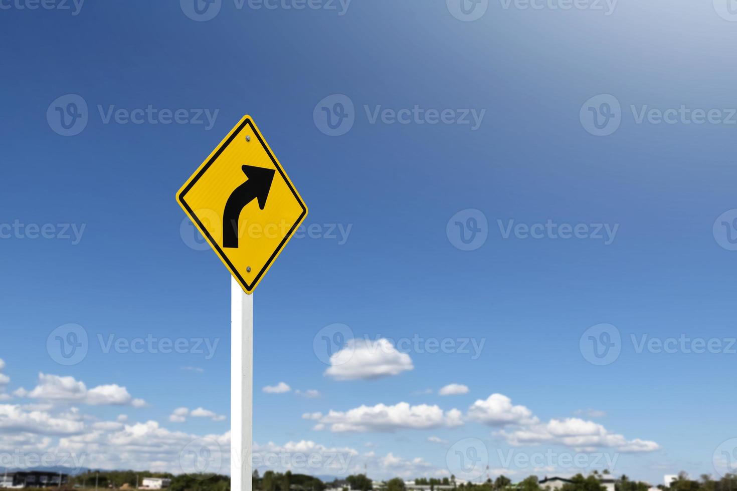 Traffic sign, left arrow curve sign on white pole by the main road with blue sky background, soft and selective focus. photo