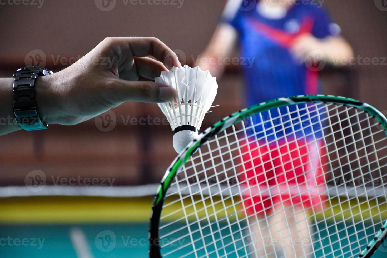 Men single badminton player holds racket and white cream shuttlecock in front of the net before serving it to another side of the court, soft and selective focus. photo