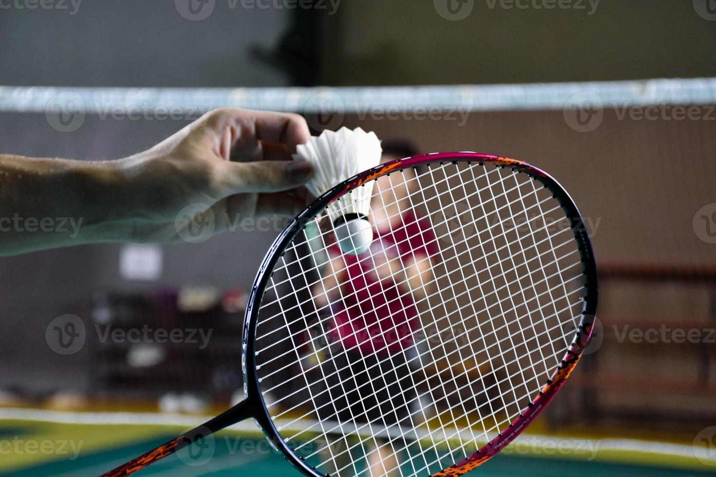 Men single badminton player holds racket and white cream shuttlecock in front of the net before serving it to another side of the court, soft and selective focus. photo