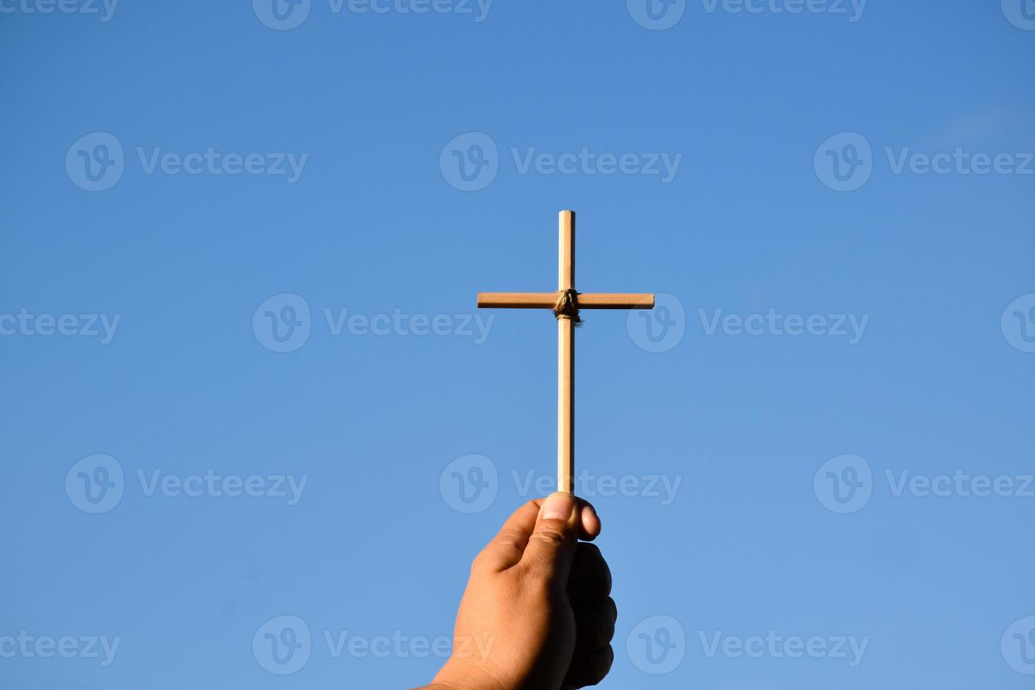 pequeña cruz de madera sosteniendo en la mano con fondo de cielo azul y nublado, concepto de amor, esperanza, verdad, fe, creer en Jesús, enfoque suave y selectivo. foto