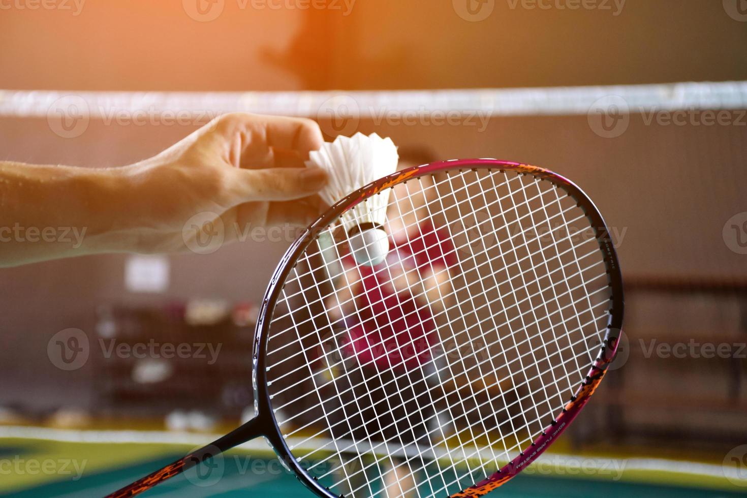Men single badminton player holds racket and white cream shuttlecock in front of the net before serving it to another side of the court, soft and selective focus. photo