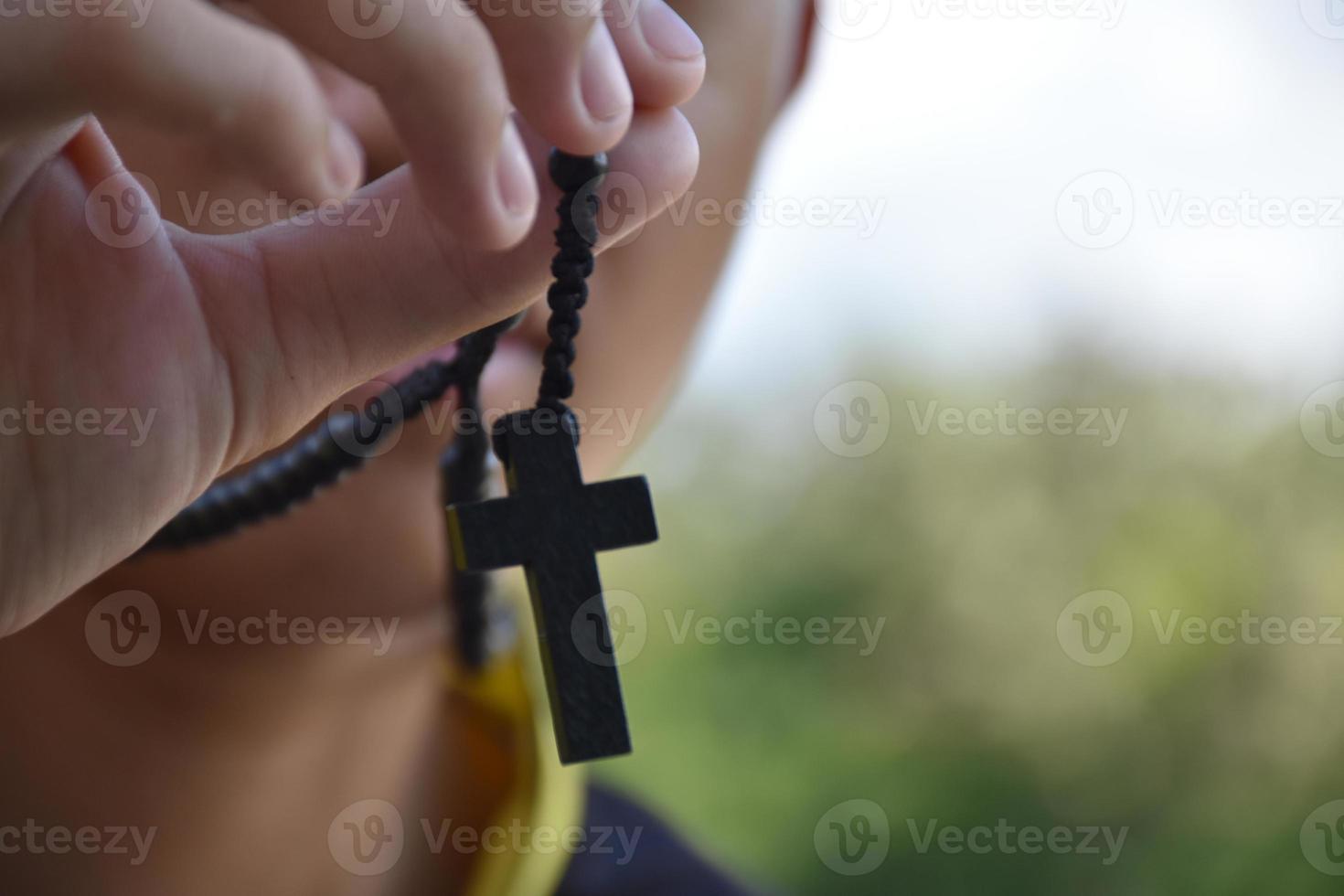 Asian young Christian boy shows his wooden rosary necklace with a cross, soft and selective focus, concept for showing pride in being a Christian to other people around the world. photo