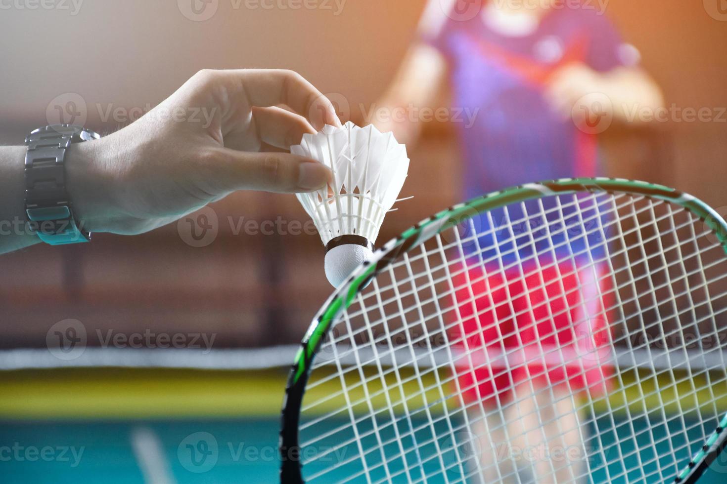 Men single badminton player holds racket and white cream shuttlecock in front of the net before serving it to another side of the court, soft and selective focus. photo