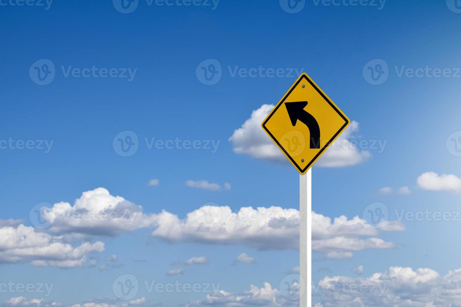 Traffic sign, left arrow curve sign on white pole by the main road with blue sky background,soft and selective focus. photo