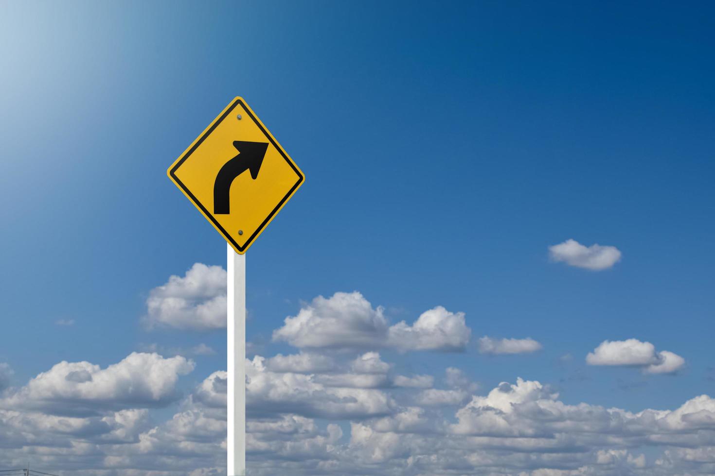 Traffic sign, left arrow curve sign on white pole by the main road with blue sky background, soft and selective focus. photo