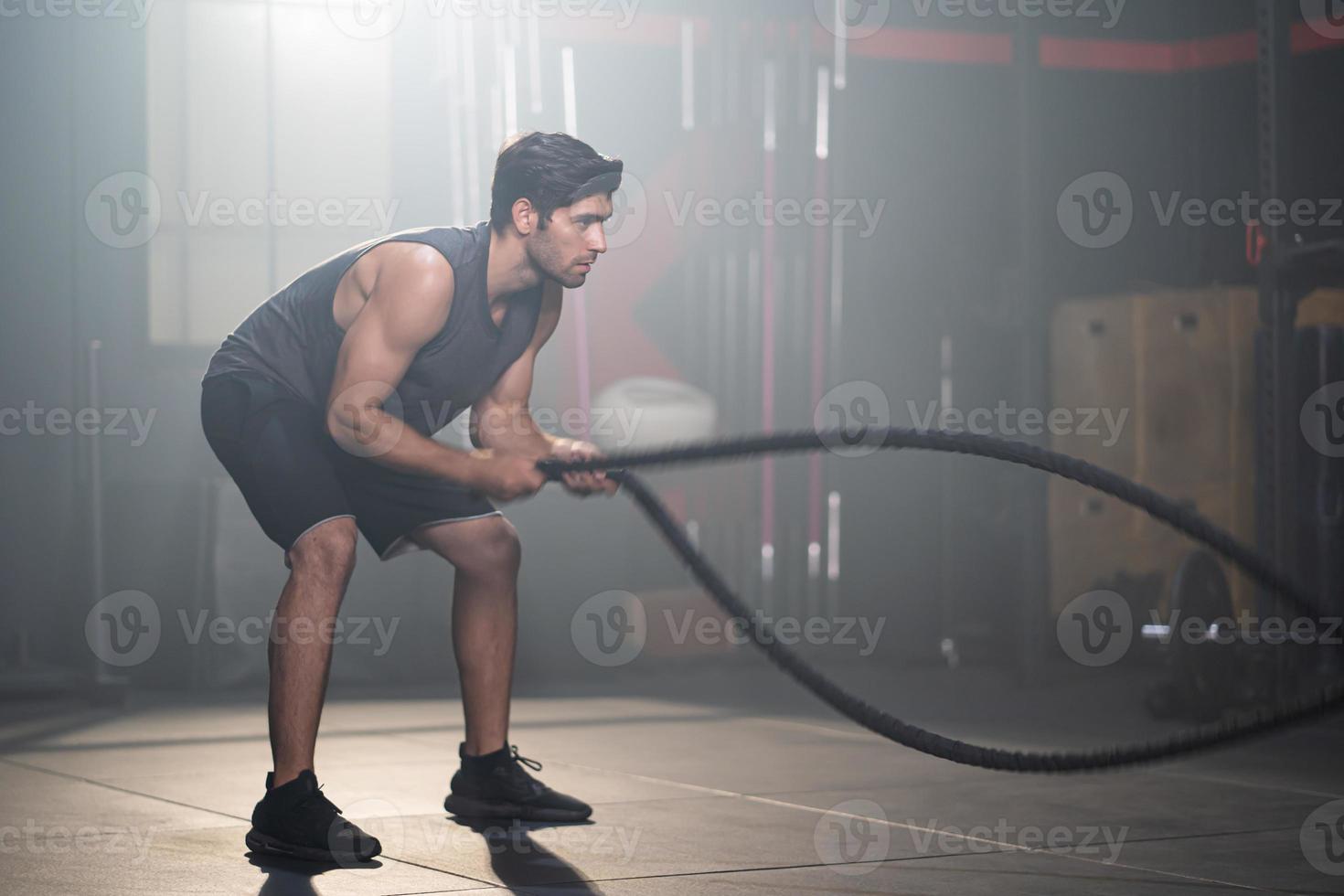 hombres caucásicos adultos guapos balancean cuerdas de batalla para hacer ejercicio cruzado dentro del gimnasio para entrenar la fuerza del cuerpo y los músculos firmes de los brazos y la buena salud física del cuerpo. foto