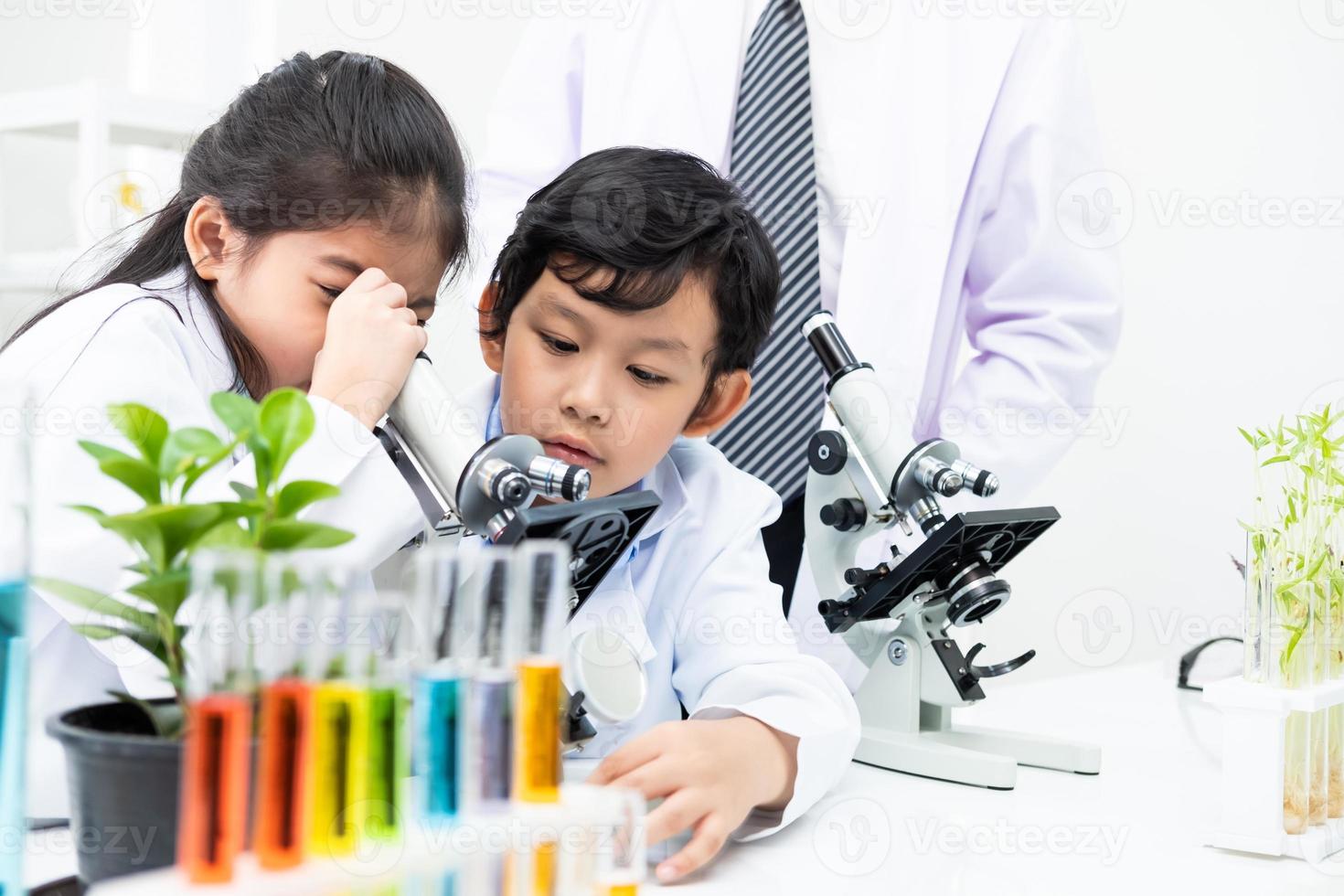 Young Asian boy and girl student wearing protective google while study and do science experiment in classroom with teacher. Learning and having fun moment. Chemist or biology classroom concept. photo