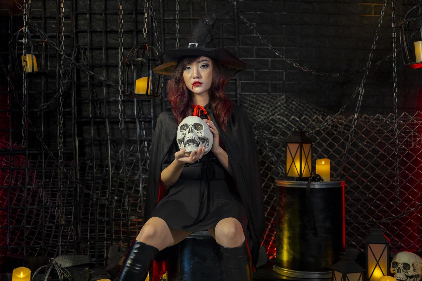 Asian girl in witch costume holding skull for halloween party trick or treat concept with dark black background with copy space photo