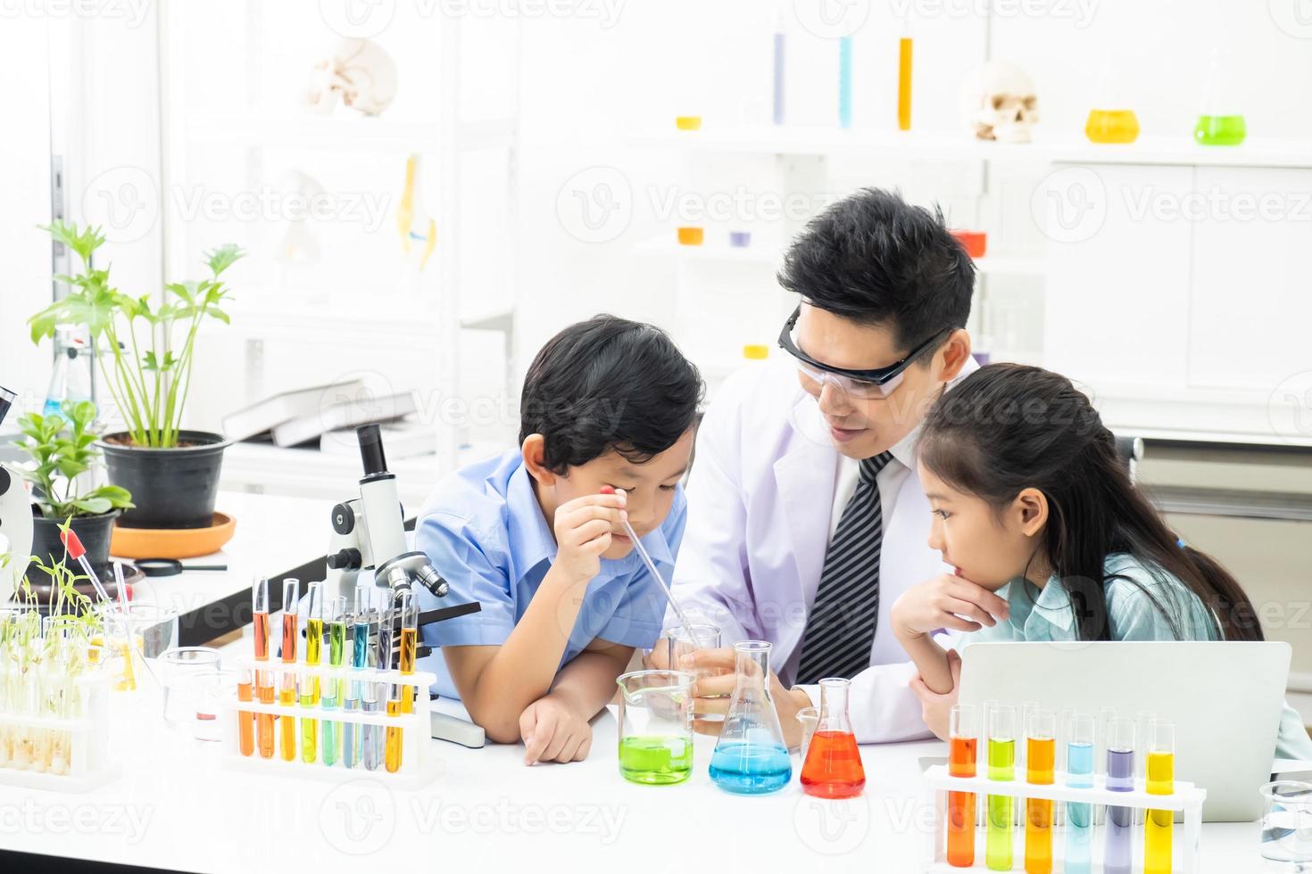 Young Asian boy and girl smile and having fun while learning science experiment in laboratory with teacher in classroom. Study with scientific equipment and tubes. Education concept. photo