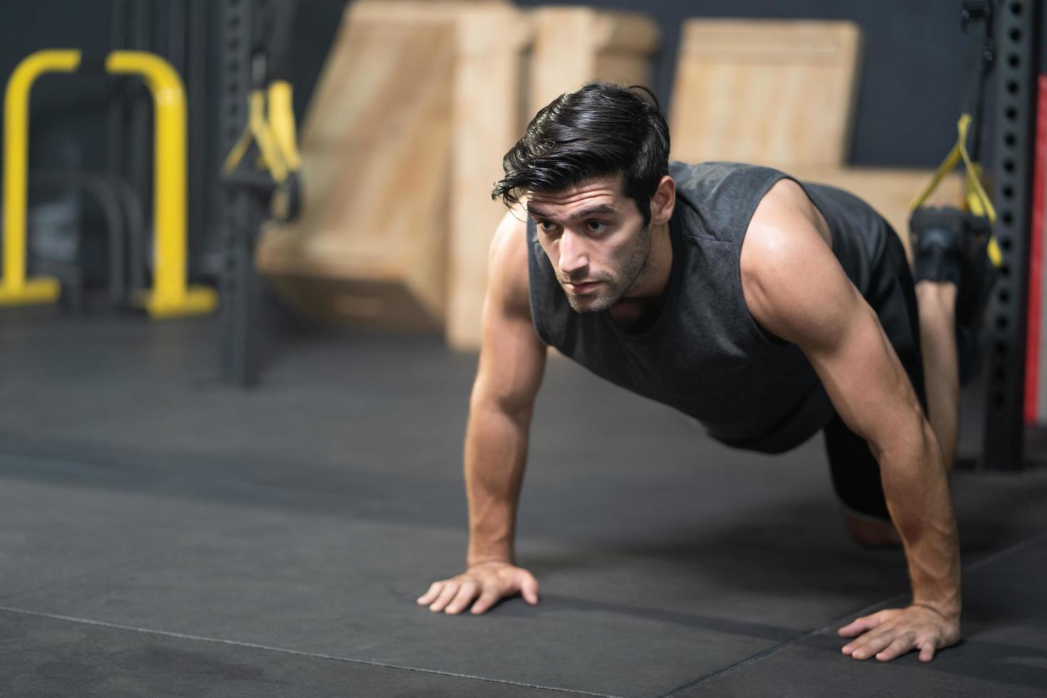 Handsome adult Caucasian men push up with trx robe to do crossfit exercise inside of fitness gym to workout for firm abs muscle and good body health. photo