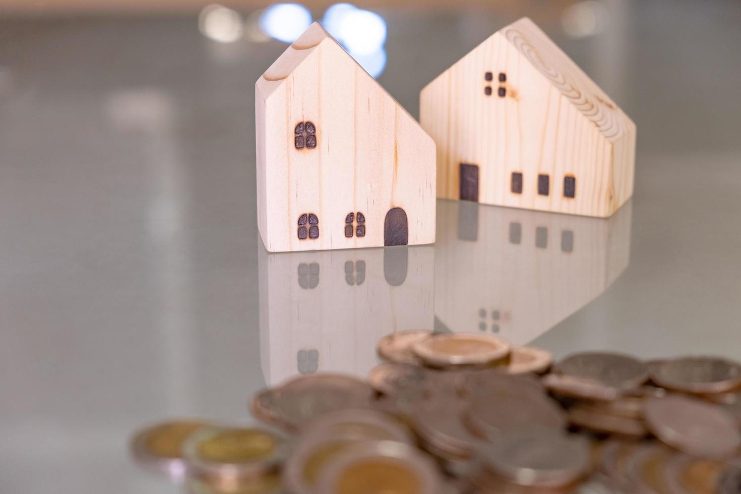 Selective focus at wooden house mock up that put on the top of growth money coins stack on the glass table with blurred background. Wealth and saving for home ownership and financial concept. photo