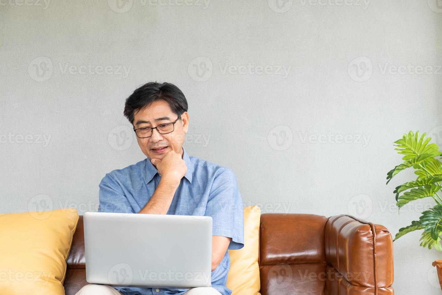 Selective focus at Old Asian men sit on the couch, having difficulty and  problem with internet and laptop computer.  Elder learning new technology or eye sight health issue. photo