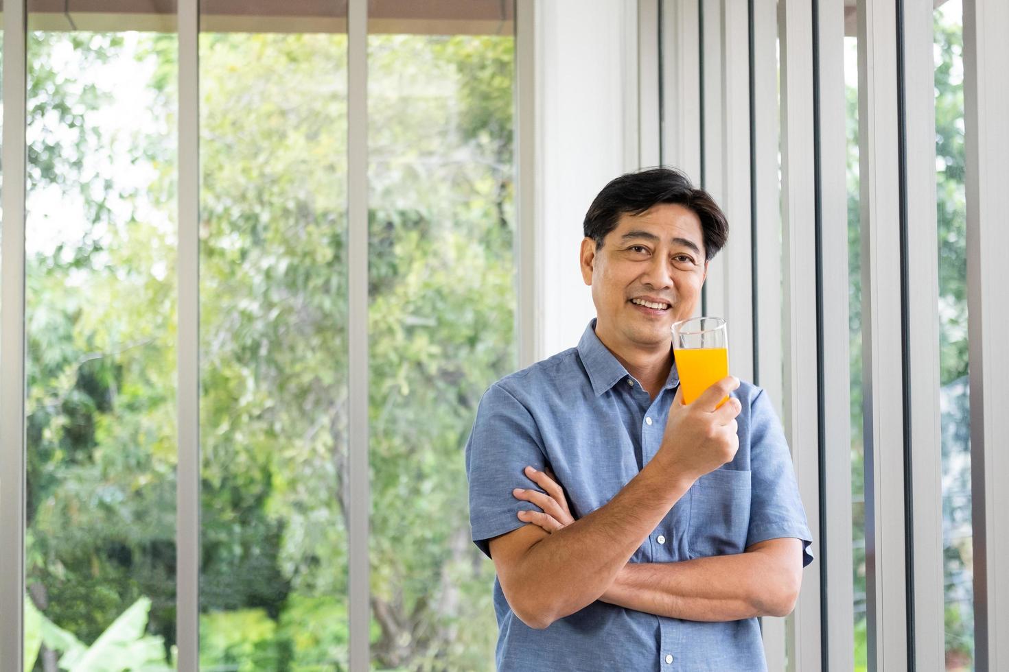 Active senior Asian man smile while holding and drink organic orange juice for breakfast. Healthy eating lifestyle for Elder people with green natural background and copy space. photo