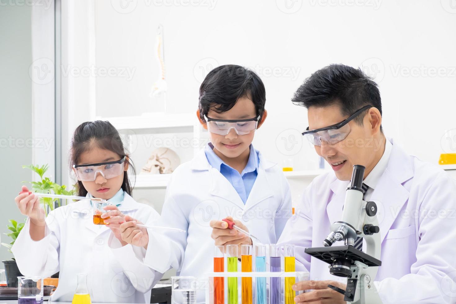 Young boy and girl doing science experiment with colorful liquid chemical inside glass tube and beaker. With teacher who teach and give instruction in classroom. Science and education concept. photo